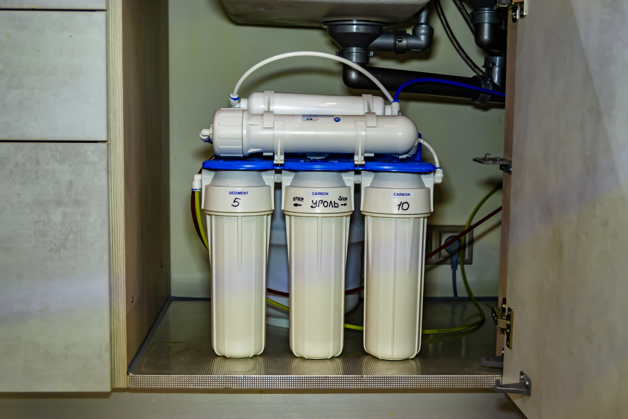 Under-sink reverse osmosis water filtration system with three vertical sediment and carbon cartridges, RO membrane on top, installed in a kitchen cabinet.