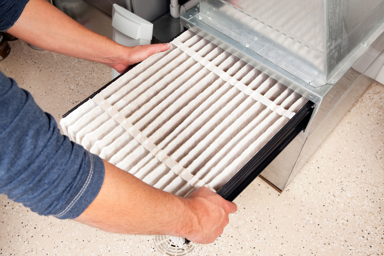 Unique Services technician sliding a new air filter into a furnace unit.