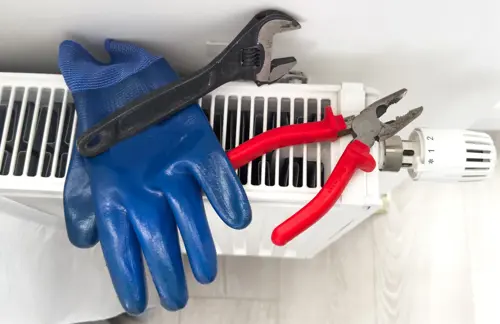 Blue work glove, adjustable wrench, and red pliers resting on a radiator heater.